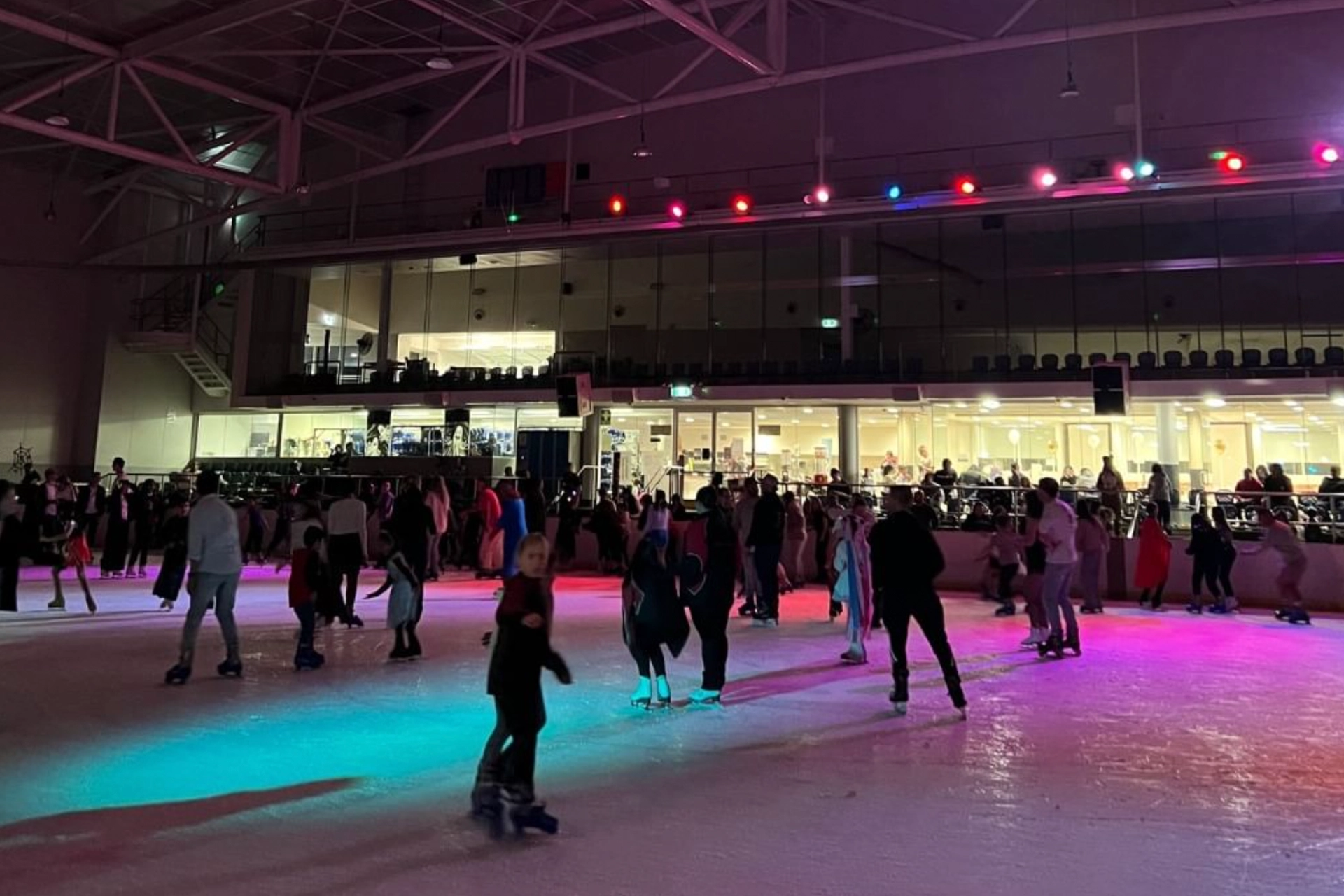 A group of people skating on an indoor ice rink.