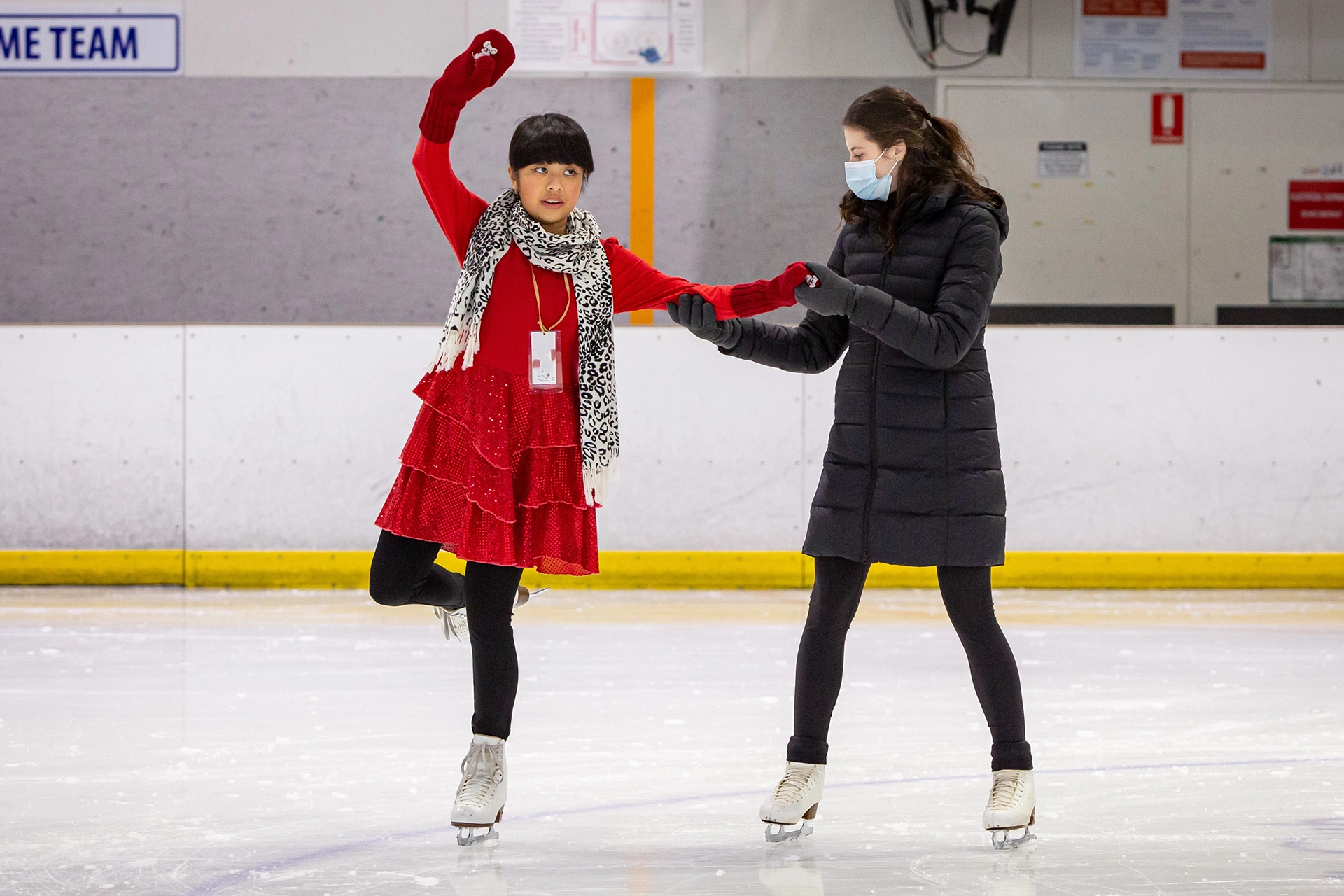 Two girls are skating on an ice rink with masks on.