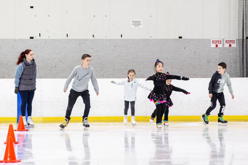 A group of children are skating on an ice rink.