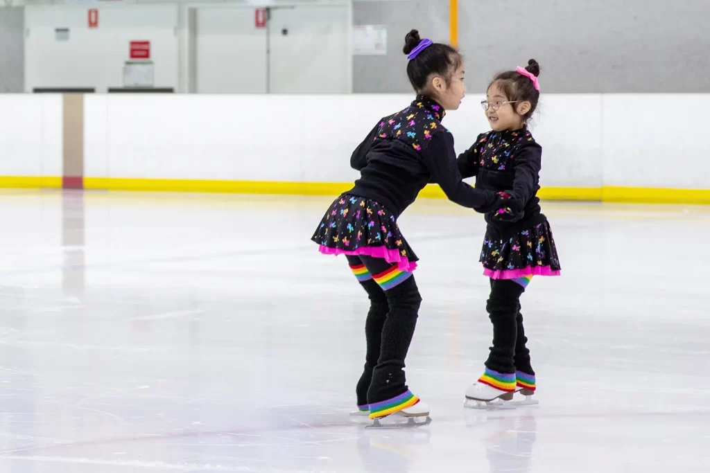 Two young girls skating on an ice rink.