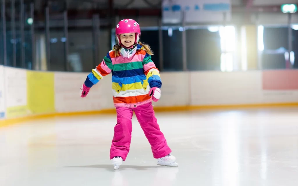 A girl in a colorful outfit skates on an ice rink.